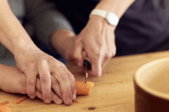 Eine Person hilft einer anderen beim Schneiden einer Karotte.