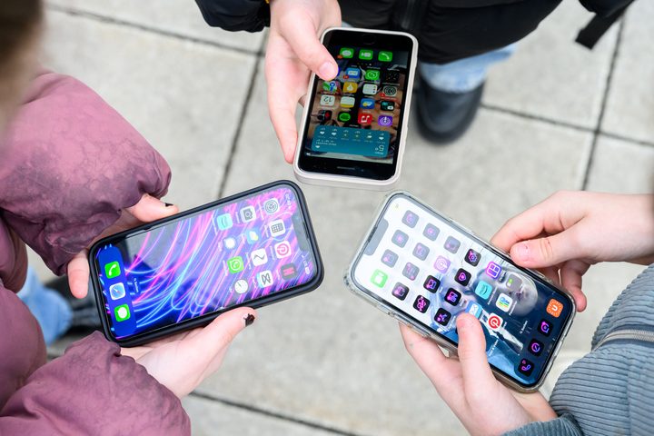 Drei entsperrte Smartphones in den Händen von jugendlichen Personen.