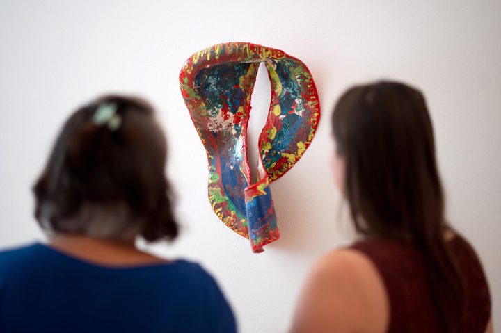Zwei Frauen stehen mit dem Rücken zu einem bunten Kunstwerk, das an einer weissen Wand hängt.
