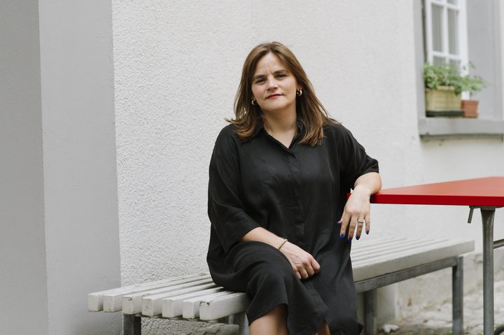 Julia Trachsel sitzt auf einer Bank an einem roten Tisch und schaut zur Kamera.